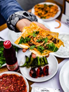 Close-up of a hand holding a flavorful shawarma wrap with assorted ingredients on a table.