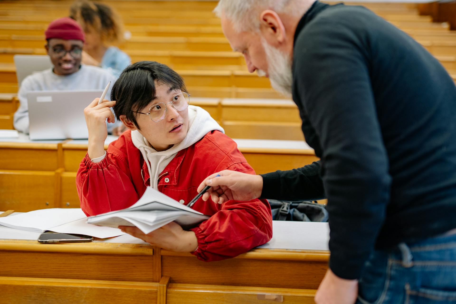 A professor assisting a college student during class in a university lecture hall.