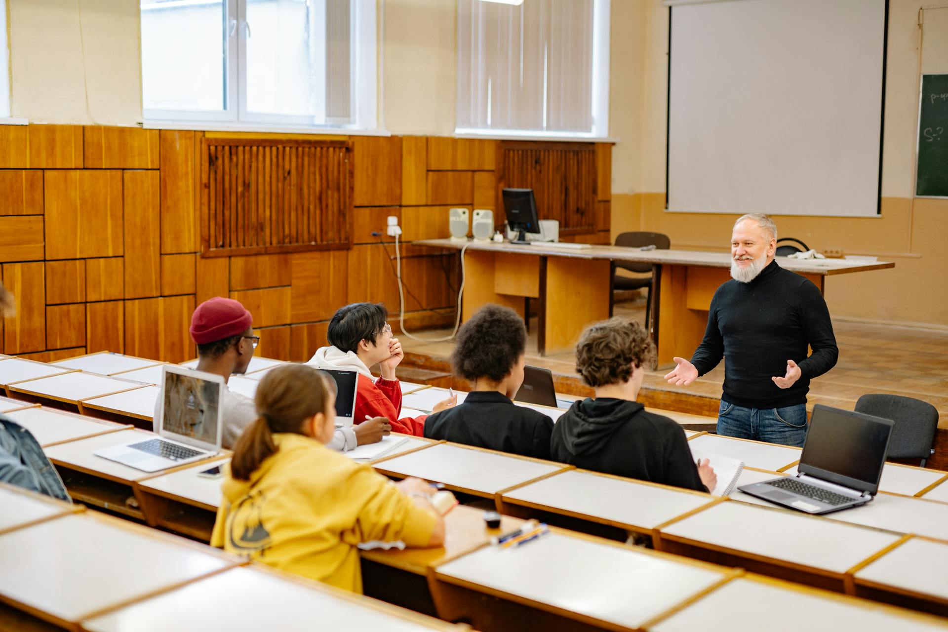 Students engaging with a professor in a university lecture hall, utilizing technology.