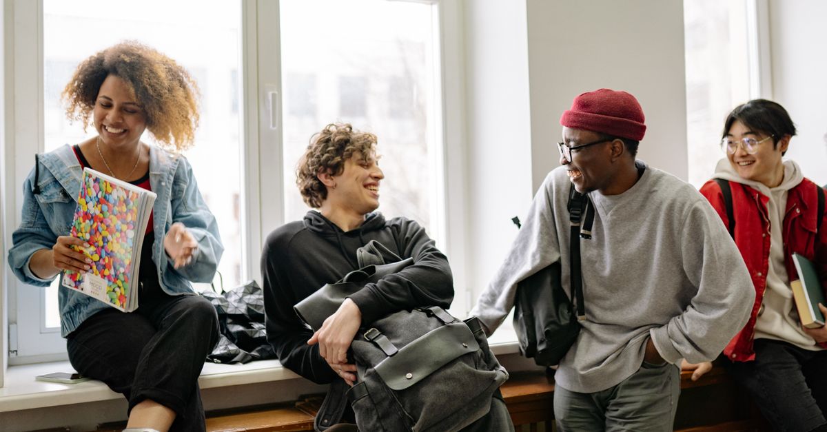 Group of diverse students laughing and studying together in a hostel common room