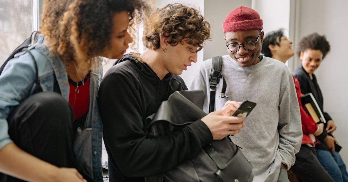 A diverse group of teenagers looking at a smartphone together, smiling and pointing at the screen