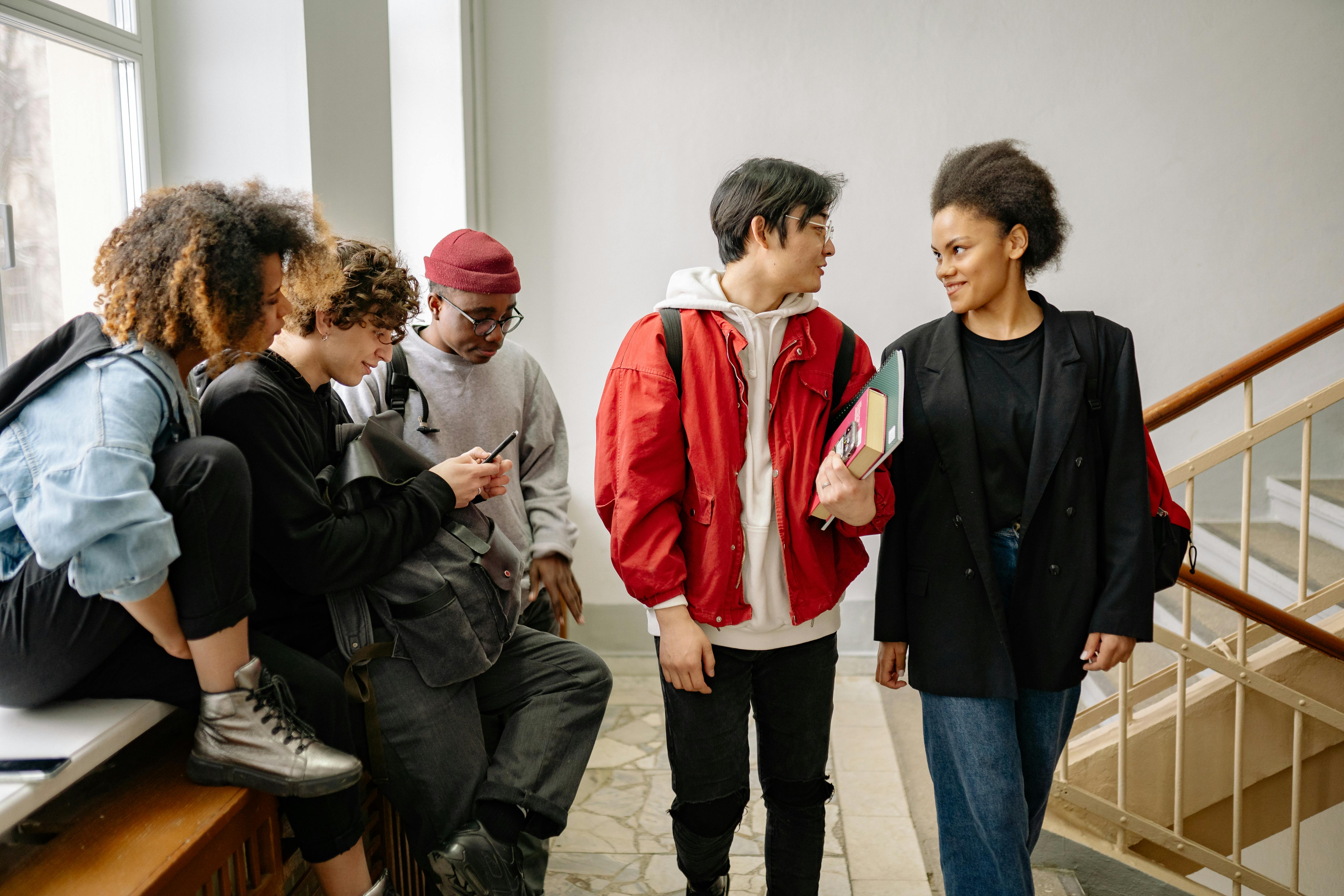 Modern bir sınıf ortamında farklı kültürlerden gelen gençlerin bir arada ders çalışarak ve sohbet ederek sosyal uyum sağladığı anı temsil eden fotoğraf.