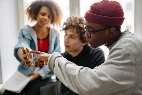 Free Three young adults discussing content on a smartphone indoors. Stock Photo