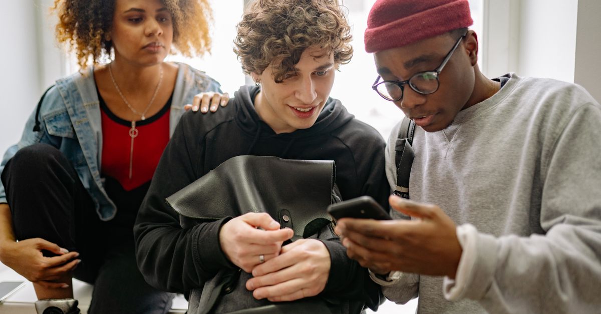 A diverse group of young friends interacting with a cellphone indoors, showcasing connection and friendship.
