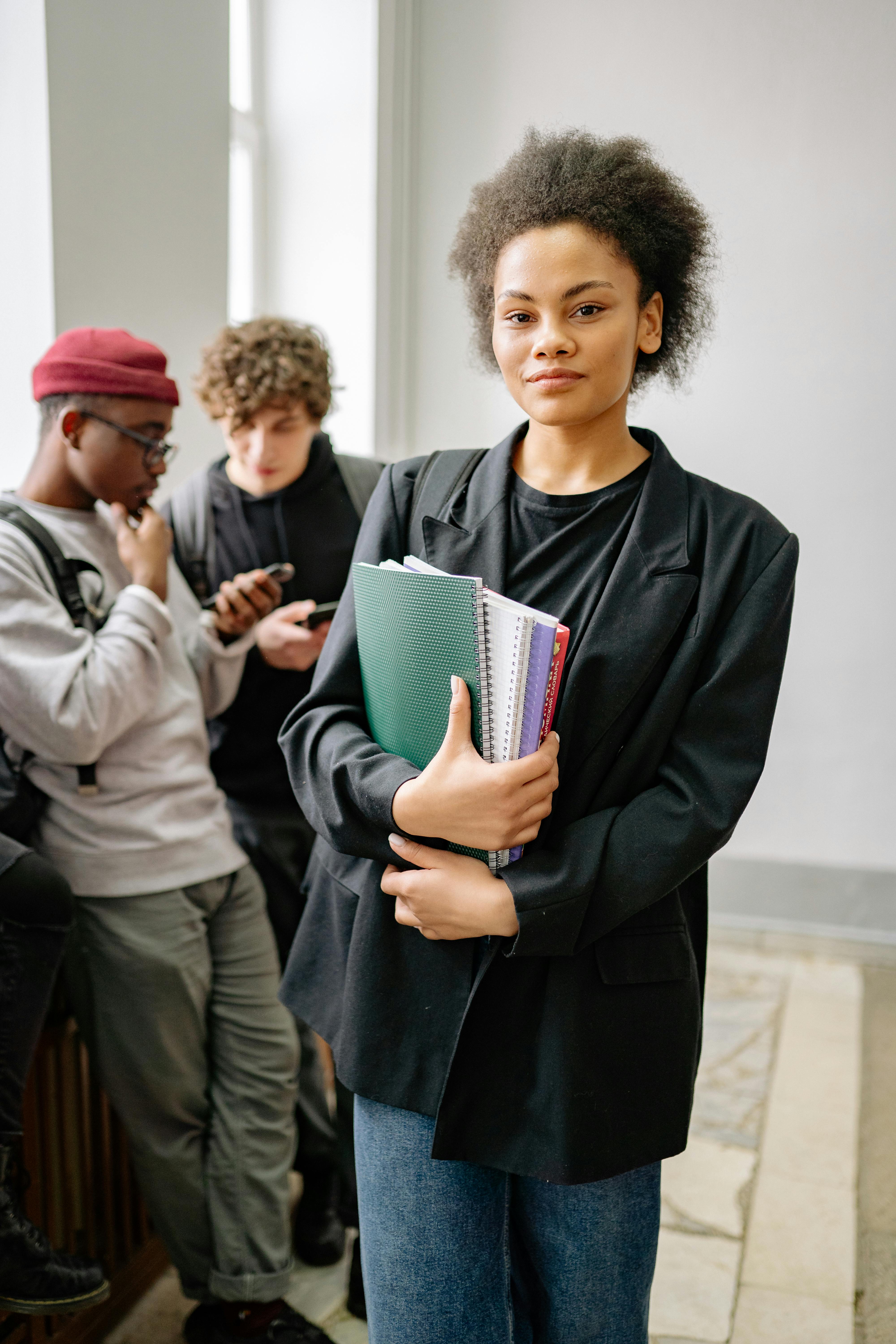 A confident student holding books in a school hallway, standing beside classmates.