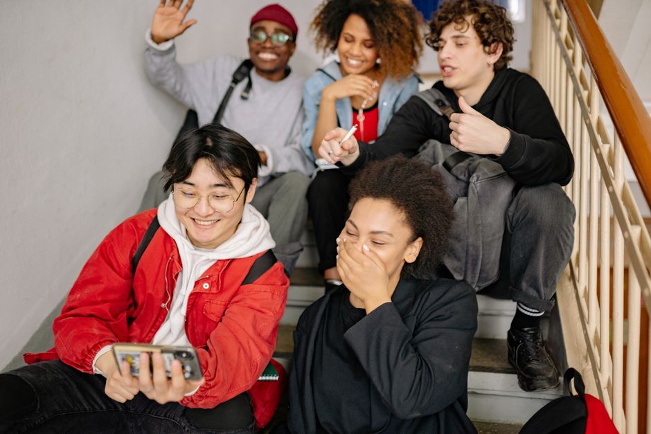 A group of teenagers sitting on stairs, laughing together while looking at a phone