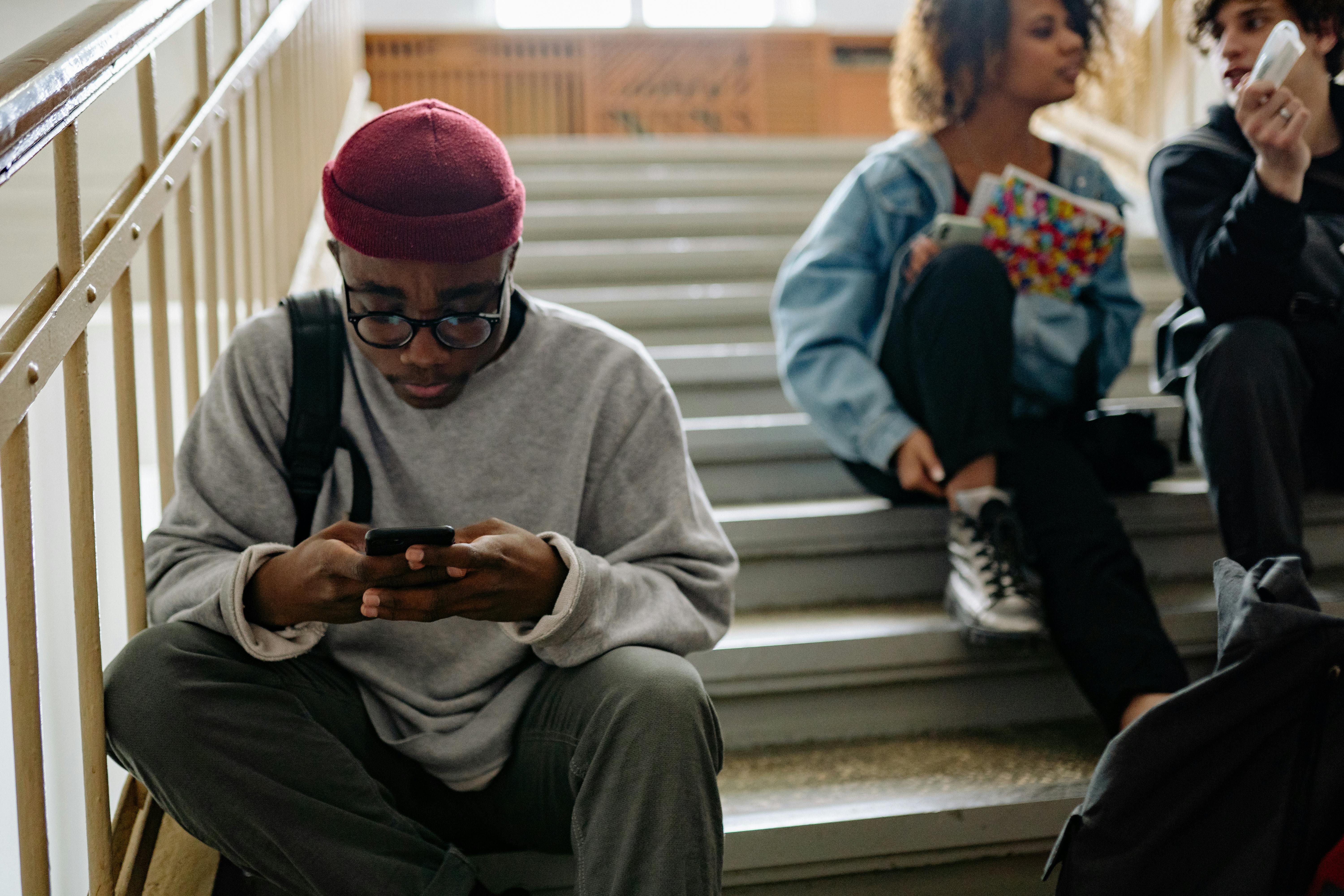 Group of young adults sitting on stairs, engaged with smartphones while relaxing indoors.