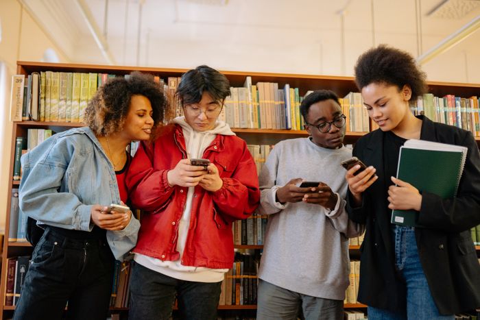 Diverse young adults holding smartphones in a university library, the age group most often searching for gen z dating apps