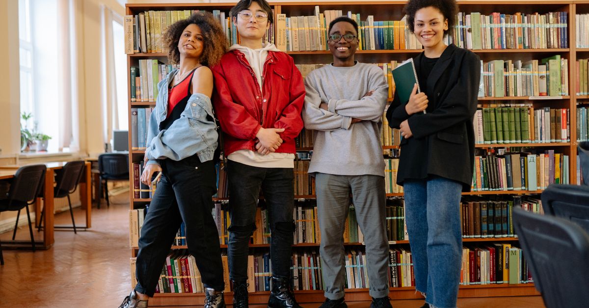 Smiling Friends Library Friends Standing Near the Bookshelves in the Library · Free Stock Photo