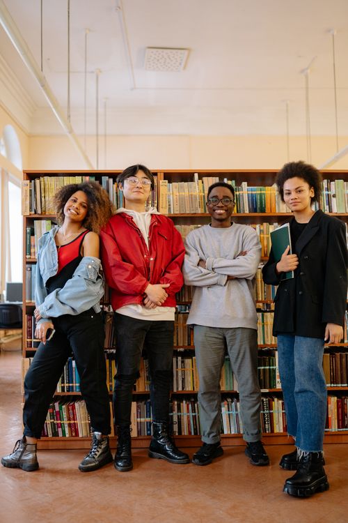 Free Young adults posing together in a library. Perfect for education and diversity themes. Stock Photo