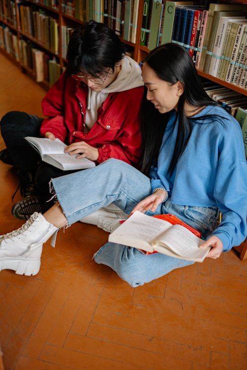 Free Two students sitting on library floor reading books, enjoying a study session together. Stock Photo
