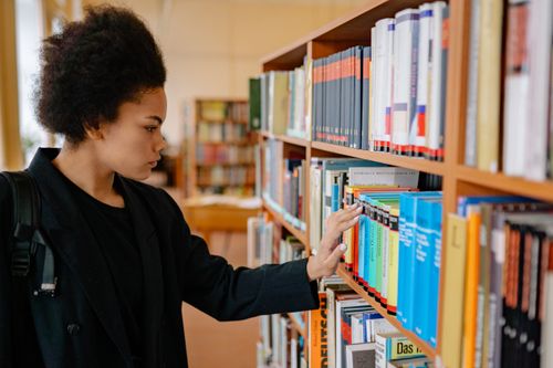Free A young woman explores bookshelves in a university library, searching for resources. Stock Photo