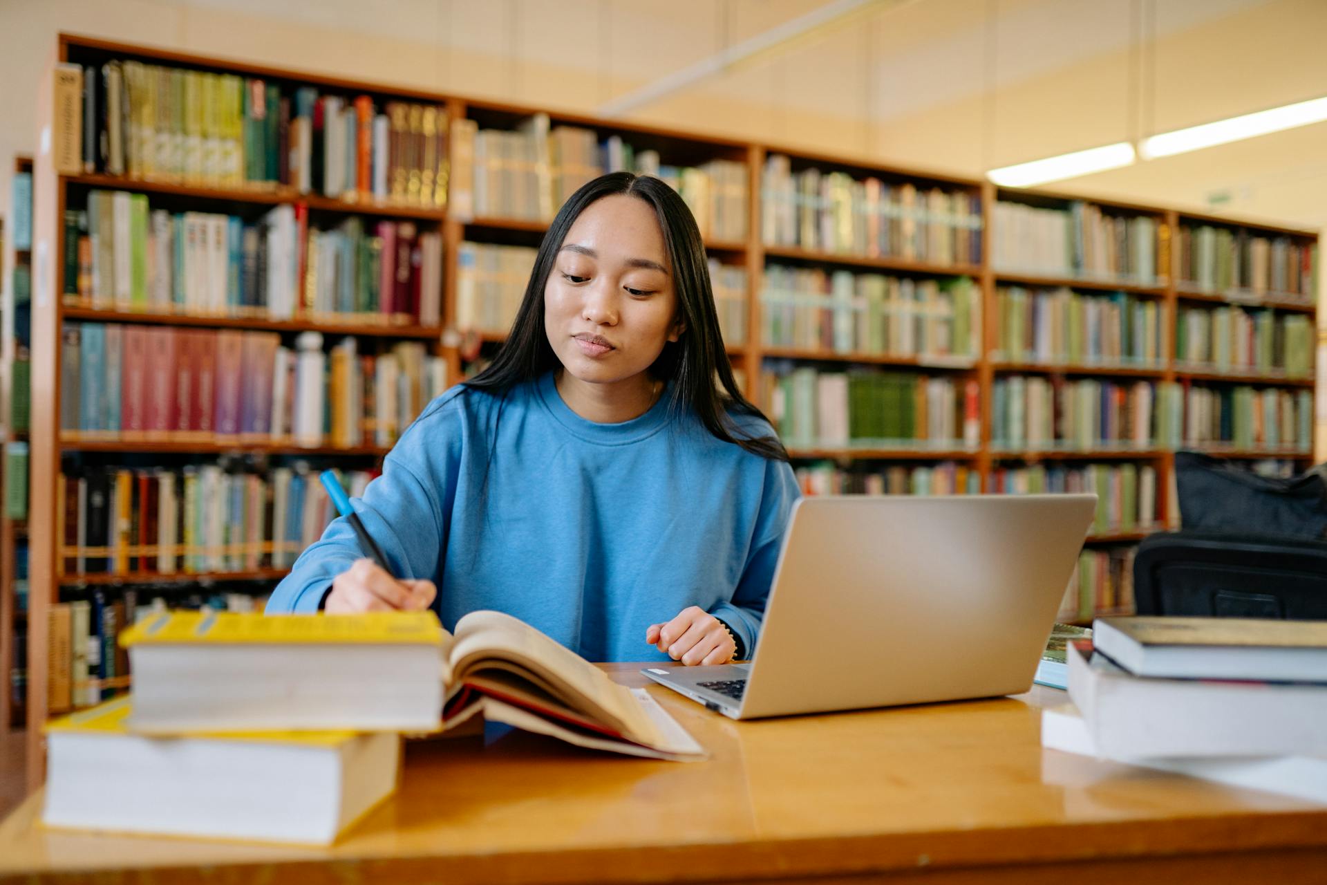 Woman in Blue Long Sleeve Shirt Sitting at the Table Writing