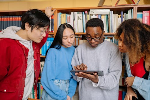 Students in a Library Looking at a Tablet Screen 