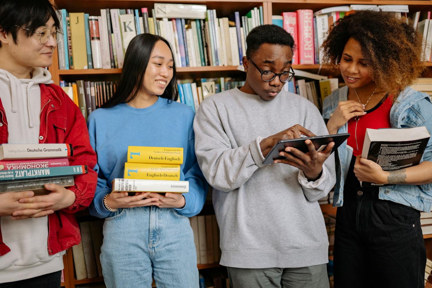 Group of diverse students study together in library with books and tablet