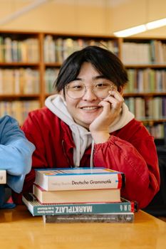 Cheerful student in a library with books, wearing eyeglasses and a red jacket.