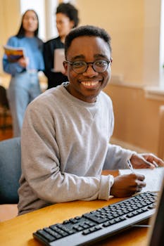 Cheerful student wearing glasses working on a computer in a classroom setting.