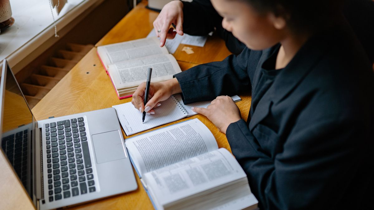 Estudiantes tomando apuntes con libros y laptop para aprender vocabulario de estudios