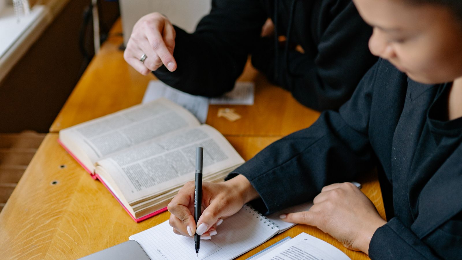 Two people with an open book and notebook at a wooden table