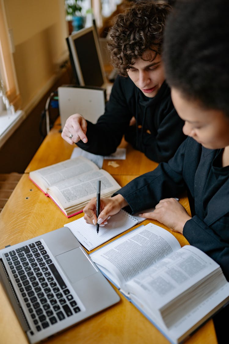 Man And Woman Studying While Writing On A Notebook