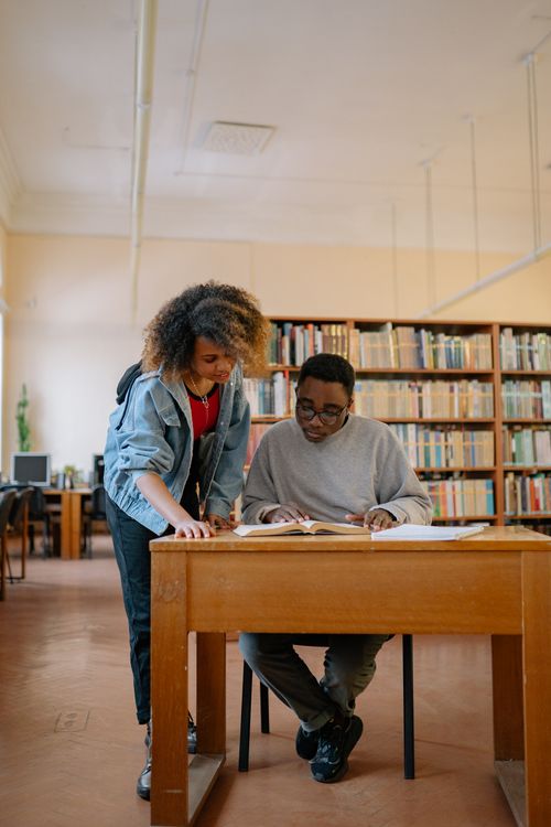Free Two university students studying together in a library, focusing on textbooks and learning. Stock Photo