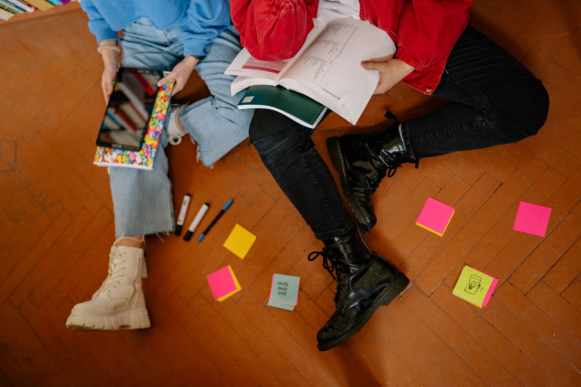 Two students studying on the floor with books, tablets, and colorful sticky notes.