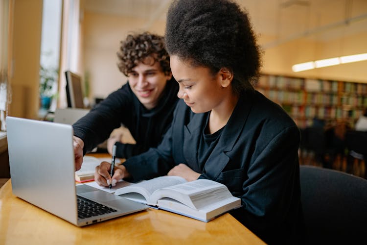 Man And Woman Studying While Writing On A Notebook