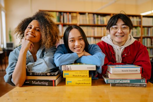 Three happy students in a library with language and marketing books.