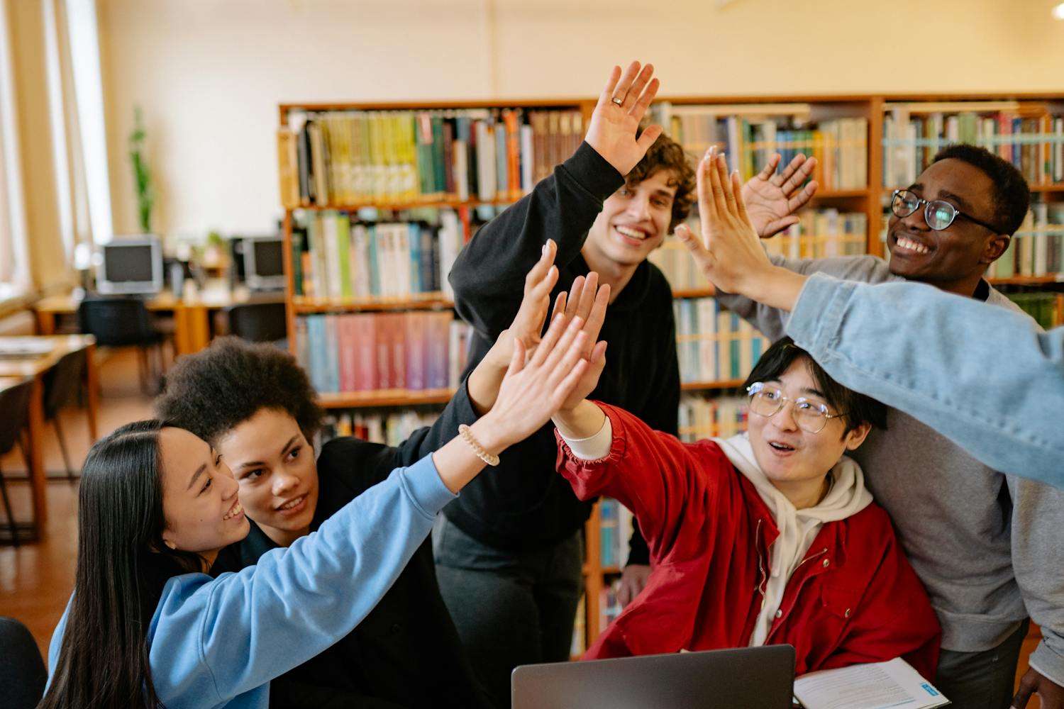 Group of happy students high-fiving in a library setting