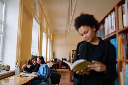 Free Students engaged in study sessions inside a university library, focusing on books and laptops. Stock Photo