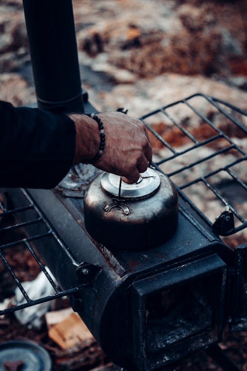 Free Side view of anonymous male tourist cooking and warming up metal kettle in portable stove while resting in camping Stock Photo