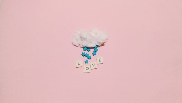 Minimalistic arrangement with cotton cloud, stars, and 'LOVE' letters on pink background.
