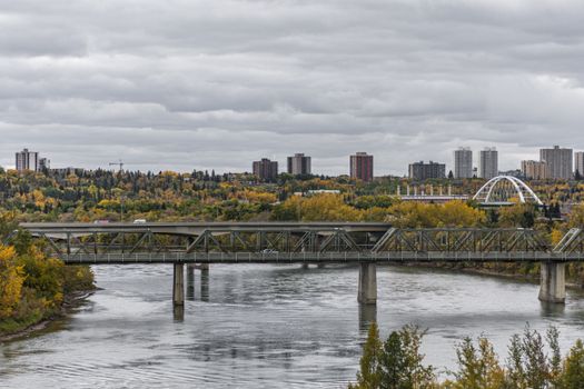 Urban skyline with a bridge over river during a cloudy autumn day, showcasing fall foliage.