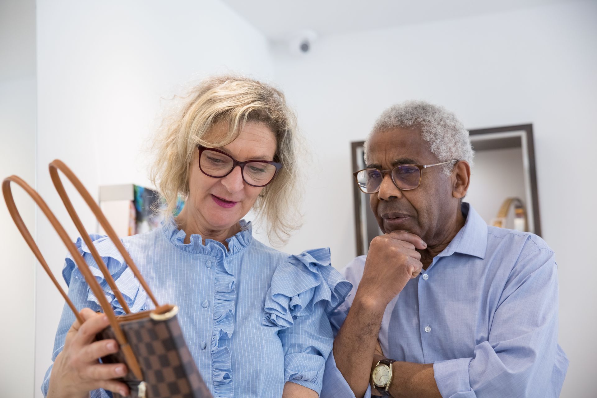 Senior couple considering a designer handbag in a clothing store, sharing thoughts.