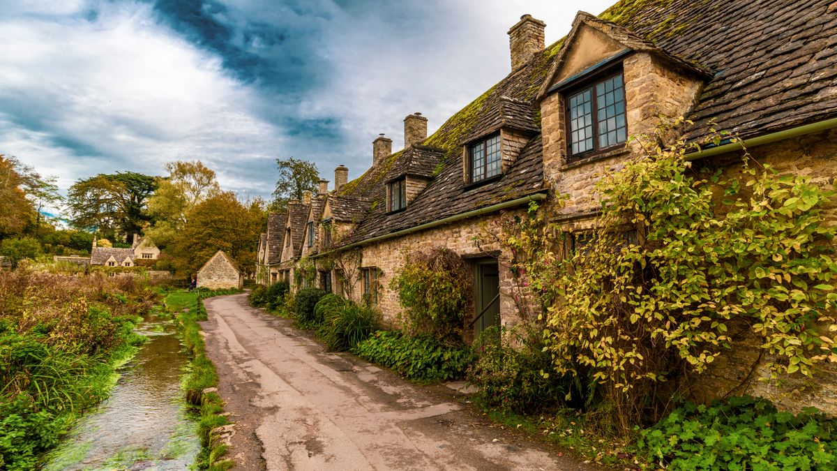 A lane beside a stream and a row of old stone cottages in Bibury in the Cotswolds