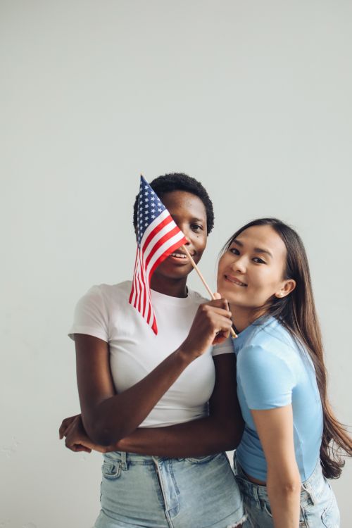 Free Two diverse women joyfully celebrate with an American flag indoors, showcasing friendship and unity. Stock Photo