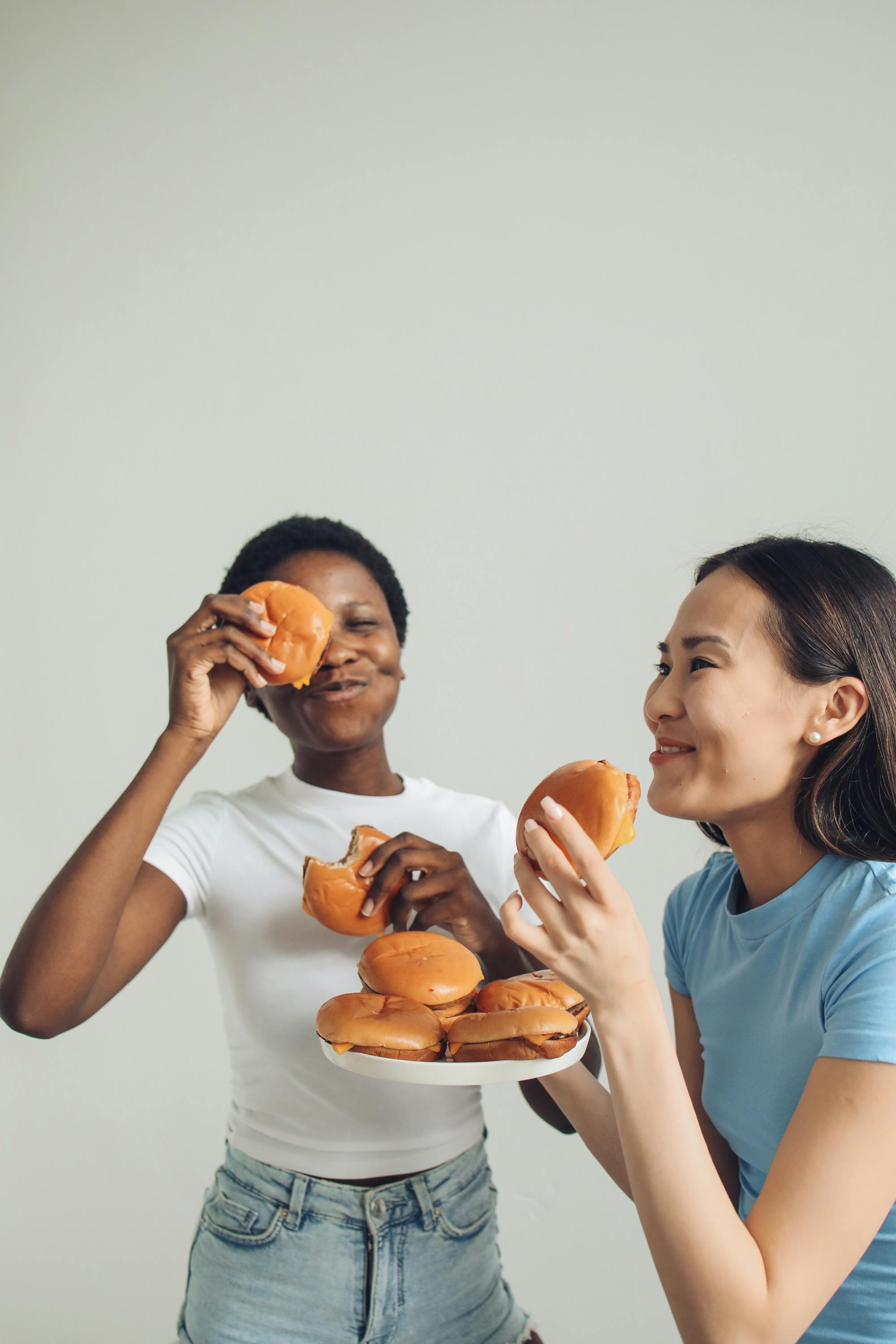 Two women having fun eating burgers together, representing friendship and enjoyment.