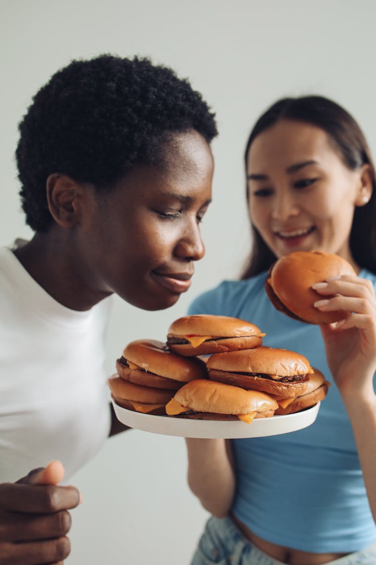 Woman In White Shirt Smelling Burgers On A Plate