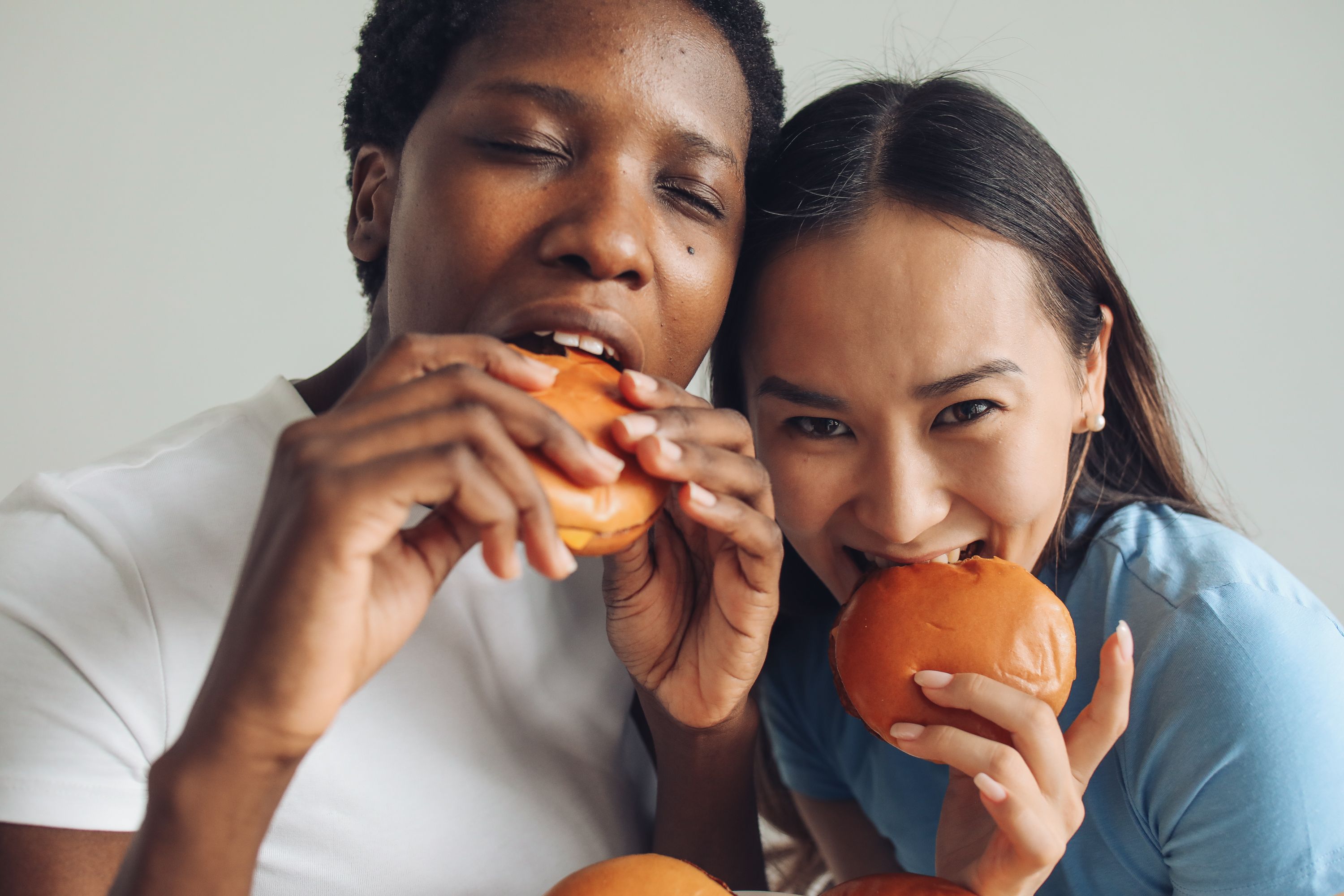 Two women happily enjoying burgers, showcasing diversity and friendship.