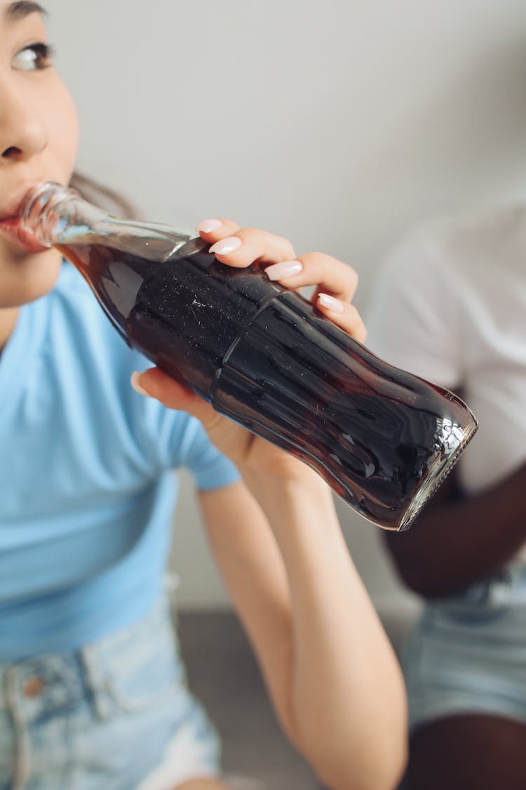 Person Drinking From Clear Glass Bottle