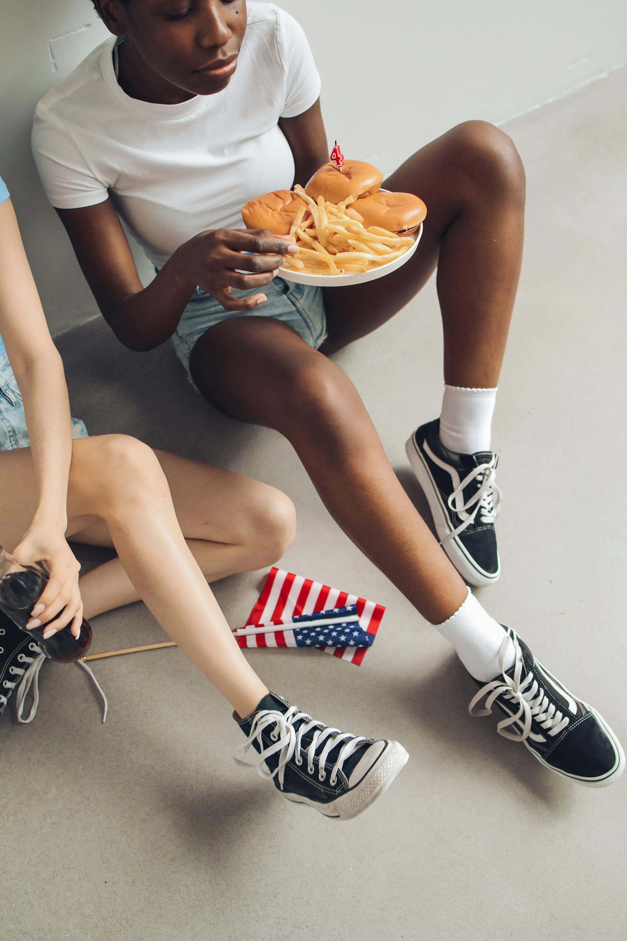 woman in white shirt and denim shorts sitting on floor with food on plate