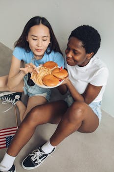 Two women enjoying burgers and fries indoors, celebrating in a casual setting.