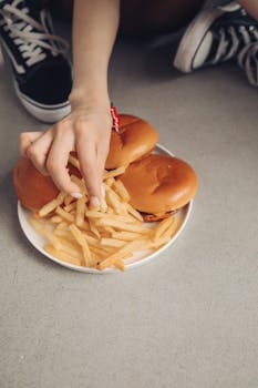 Close-up shot of a hand grabbing fries from a plate with burgers. Casual dining scene.