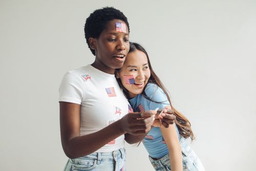 Free Two friends joyfully celebrating Independence Day with American flag stickers and casual wear. Stock Photo