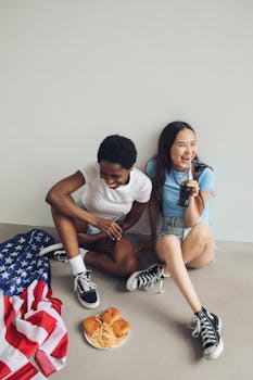 Two young women enjoy burgers and cola while celebrating with an American flag indoors.