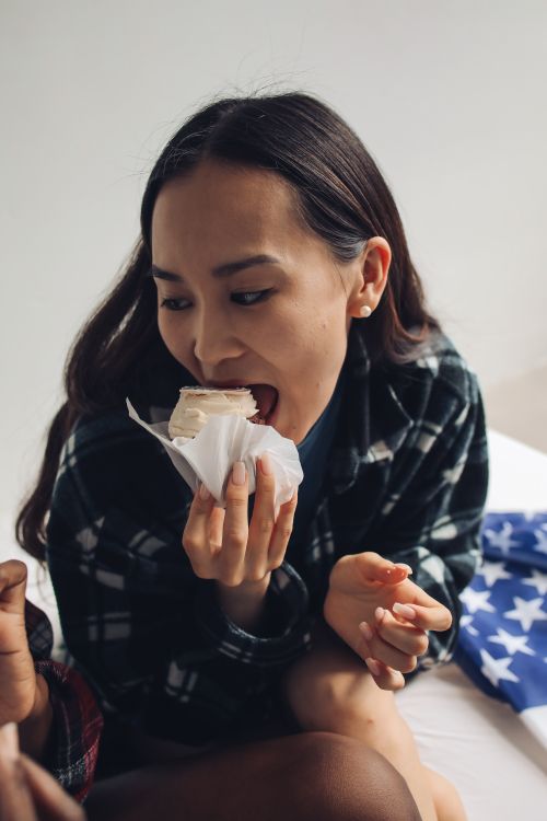 Free Young woman biting into a cupcake with a stars pattern in the background, celebrating indoors. Stock Photo