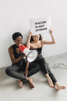 Two women sitting, protesting with a sign and megaphone against racism.