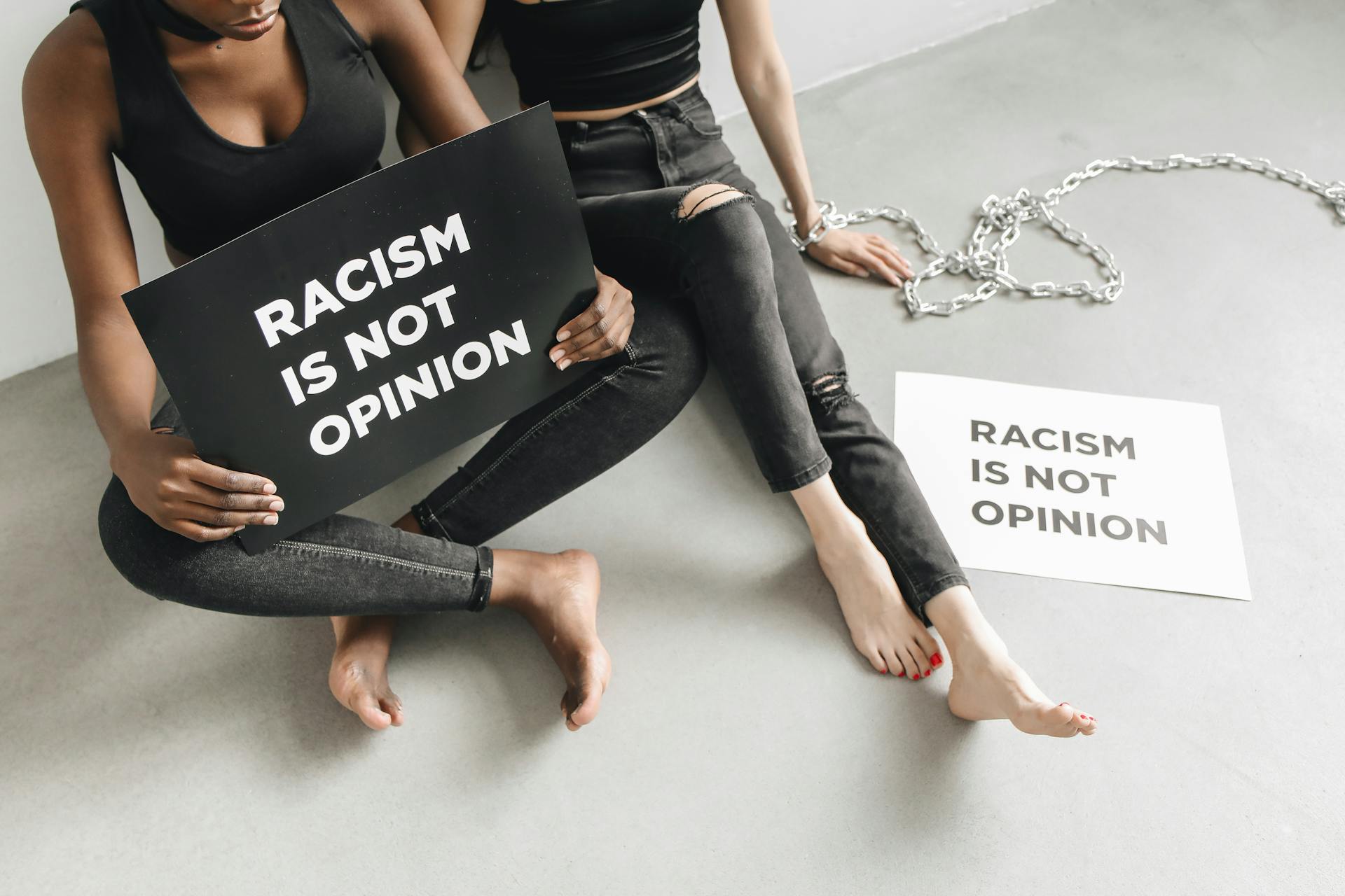 Two women holding signs stating 'Racism is not opinion' during a protest indoors.