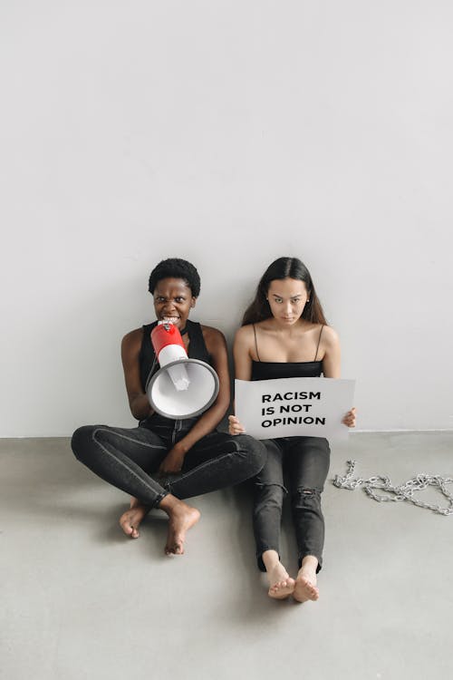 Free Two Women Sitting on the Floor While Holding a Signage and Megaphone Stock Photo