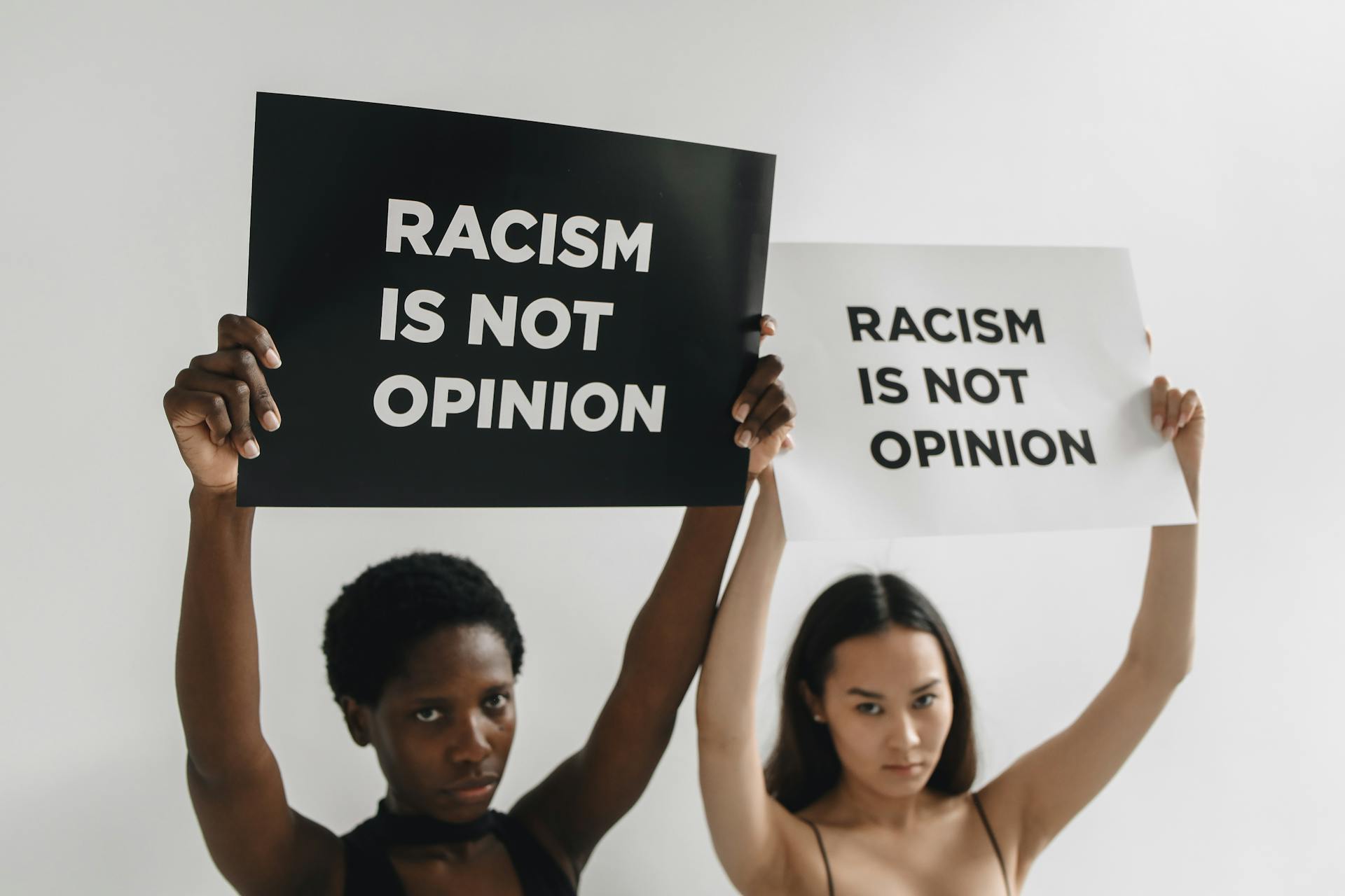 Two women hold signs that read 'Racism is Not Opinion' advocating for racial equality.